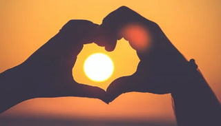 Händer som formar ett hjärta runt solen – symbol för kärlek, intimitet och förspel
