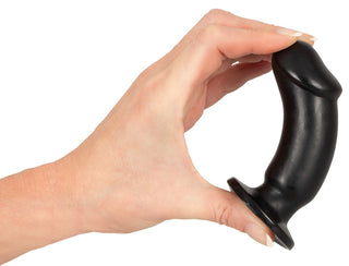 En hand håller ett föremål från Analsex Training Set, med en svart, böjd design med en utsvängd bas och sugkopp, mot en vit bakgrund.