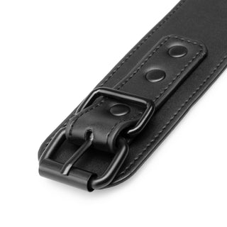 Närbild på Halsband & Handledsbojor: ett svart läderband med metallspänne och sydda kanter, perfekt som ett elegant justerbart halsband eller för användning vid BDSM-lek.