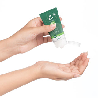 Någon pressar Aloe Vera Bio Glidmedel 100ml från en grön tub till sin öppna handflata mot en vit bakgrund.
