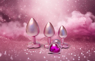 Gleaming Love Pearl Pink Buttplug Set, med metalliska rosa pluggar med hjärtbaser och hjärtformade ädelstenar, kompletteras perfekt av en gnistrande rosa bakgrund för perfekt analstimulering.