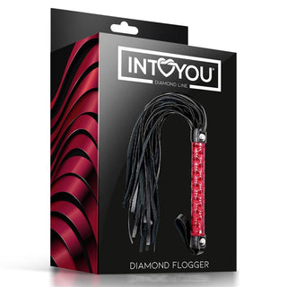 En box med Diamond Vegan Leather Flogger med svart och rött handtag, tillverkad av veganskt läder, visas mot en vågig röd bakgrund.