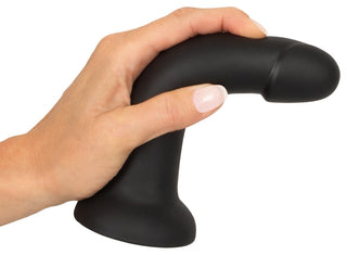 En hand håller Strap-on Trosor med Dildo, en svart silkeslen silikondildo med en expertkurva för G-punkts- eller prostatastimulering, mot en vit bakgrund.