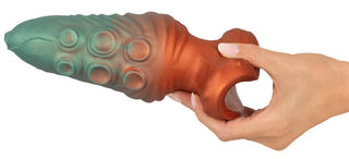 En hand håller i Beasty Cocks Atlantis Buttplug, en texturerad, tvåfärgad fantasileksak i flytande silikon med cirkulära mönster och fingergrepp.