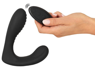 En hand håller i en svart fjärrkontroll bredvid Intense Prostata Vibrator RC, en elegant L-formad prostataplugg i silikon, på en vit bakgrund.