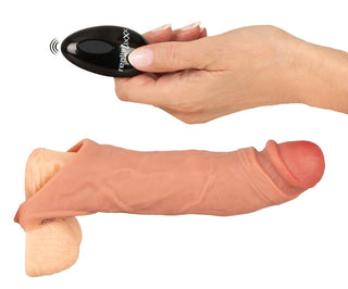 En hand håller en fjärrkontroll nära Vibro Sleeve med Ballring, perfekt för att förlänga penis eller para ihop med en vibrator med fjärrkontroll.