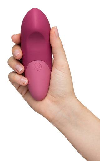 En hand håller en rosa, droppformad enhet med en knapp, liknande den eleganta designen hos Womanizer Vibe Klitorisvibrator.