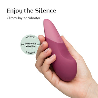En hand håller en lila Womanizer Vibe Klitorisvibrator, vilket framhäver dess tysta UltraWave-teknologiska vibrationsfunktion.