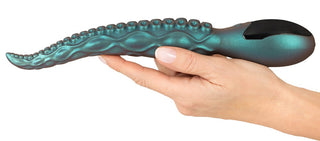 En hand håller Octo Vibes Tentacle Vibrator, en blågrön leksak med en tentakelinspirerad design och upphöjda bulor längs längden.