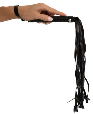 En hand greppar Magic Shiver Flogger, ett svart BDSM-tillbehör i läder med flera tofsar, mot en vit bakgrund, vilket framkallar en air av dominans och mystik.