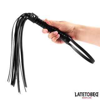 En hand som håller i Latetobed Flogger 52 cm, ett BDSM-tillbehör i svart läder med flera svansar och en handledsrem för varierad stimulering.