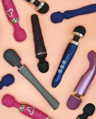 Flera olika wand massagers i olika färger, inklusive rosa, blå och svarta modeller, arrangerade på en ljus orange bakgrund.