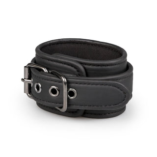 Bondage set till sängen: Svart läderarmband med justerbara remmar, metallspänne och öljetter på vit bakgrund.