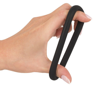 En hand håller elegant en svart oval gummiring, som liknar den eleganta Black Velvet Cock & Ball Loop, med fingrarna graciöst utsträckta.