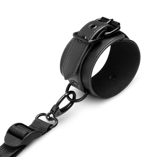 Under the Bed Restraint Set, med en svart lädermanschett med spänne och rem, är perfekt för entusiaster av bondagelek, vackert visad på en orörd vit bakgrund.