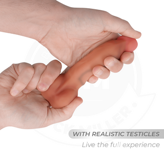 En hand håller Cock Miller Böjbar Dildo 15cm med testiklar, tillverkad av medicinskt silikon. Den böjbara designen ger en naturtrogen känsla.