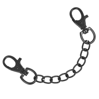 De veganska fotledshandbojorna i läder, med stora ovala länkar och ett spänne i varje ände, erbjuder en elegant bondage-estetik. Deras svarta metallkedja kröker sig något, framhävd mot en vit bakgrund med en blank, slät yta.