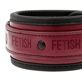 En närbild av Vegan Leather Ankel Handcuffs visar ett rött veganskt läderband med svarta kanter, prydd med svarta nitar och djärvt visar ordet "Fetisch" med en slät, glansig textur som påminner om bondage-lekar-tillbehör.