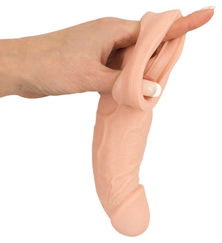 En hand håller produkten "Penisförlängare - Nature Skin" som är ett stretchigt silikonobjekt som liknar en realistisk fallisk form, perfekt som en penismuff.