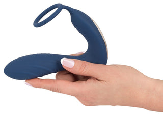 En hand håller Prostata Vibrator Med Penisring - Fjärrkontroll, med en blå silikonpenisring med två eleganta öglor.