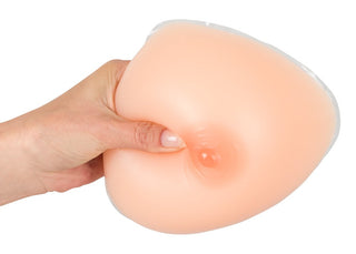En hand som klämmer på Lösbröst Av Silikon illustrerar dess mjukhet och flexibilitet och framhäver dess realistiska känsla för bystförstoring. Protesen är ljusbeige.
