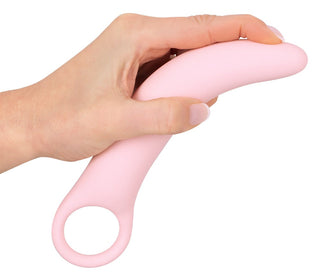 En hand håller graciöst en rosa silikonleksak, designad med ett svängt och bekvämt fingerhål – perfekt för bäckenbottenträningar eller för användning tillsammans med Vaginal Trainers Set.
